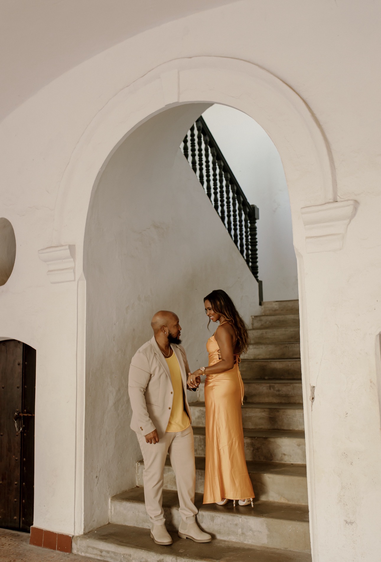 Andrew and his wife holding hands on a stone staircase beneath an arch
