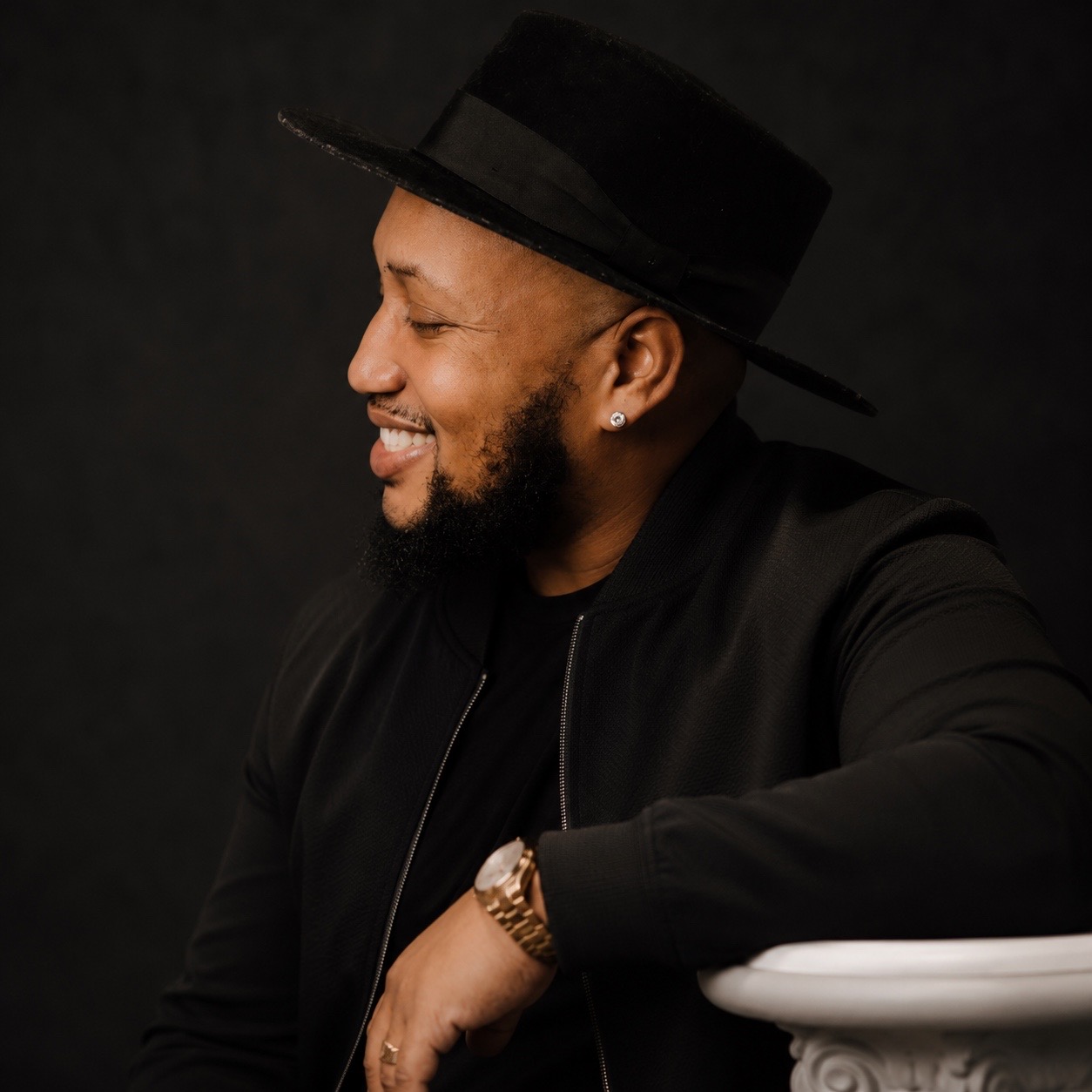 Andrew Alleyne in a black wide-brimmed hat, smiling in a studio portrait