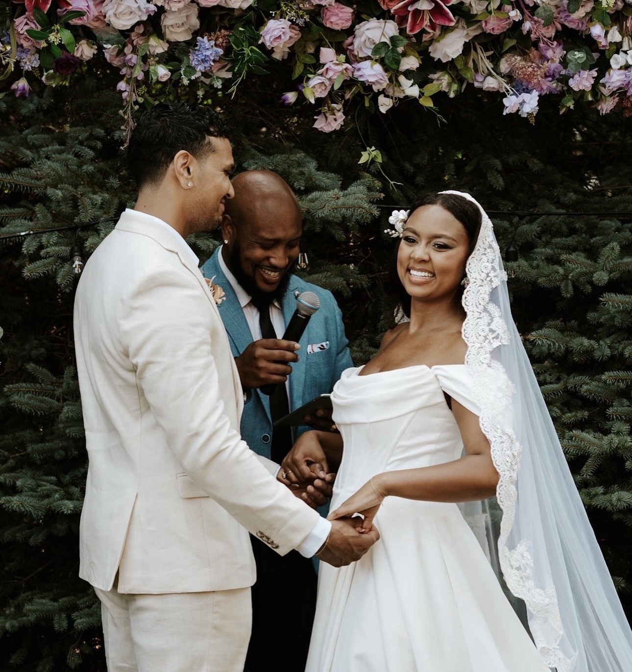 A couple holding hands and laughing as Andrew Alleyne leads their vows