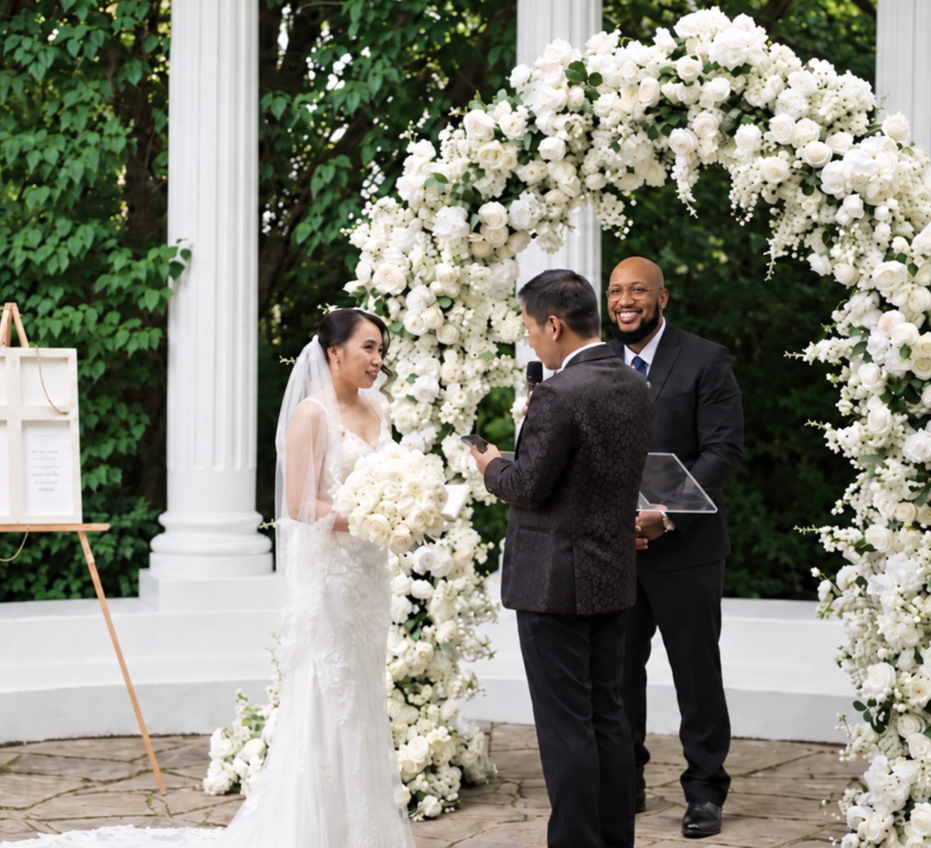 Andrew Alleyne officiating a garden ceremony beneath a white floral arch