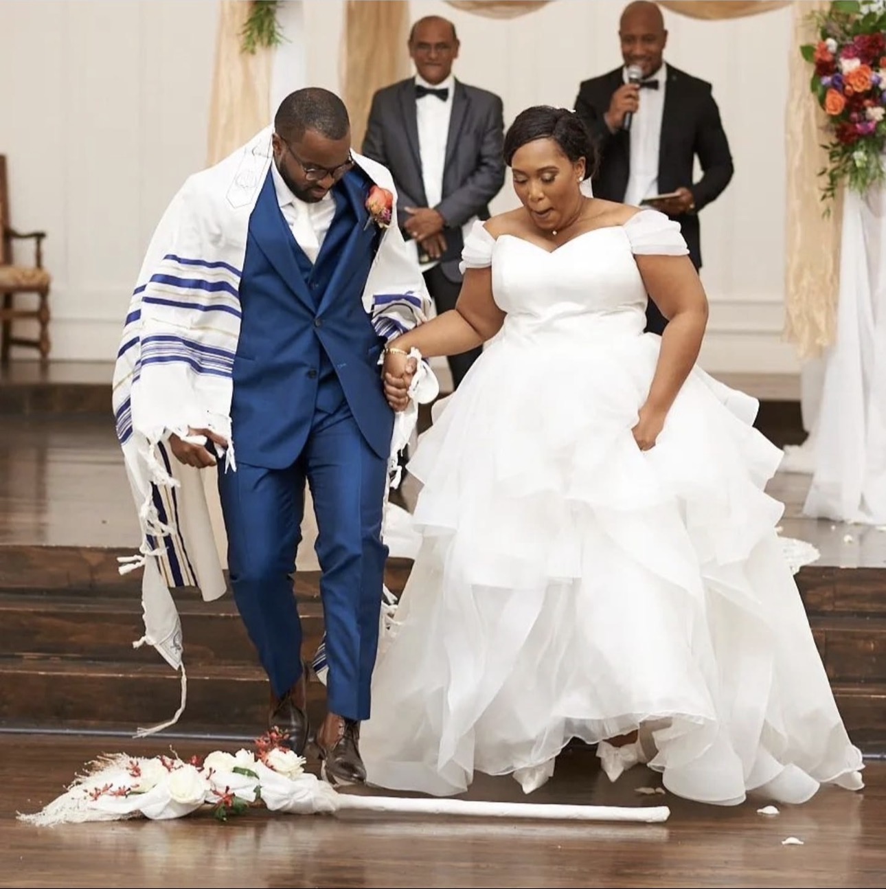 A newlywed couple jumping the broom as Andrew Alleyne leads the moment from the altar