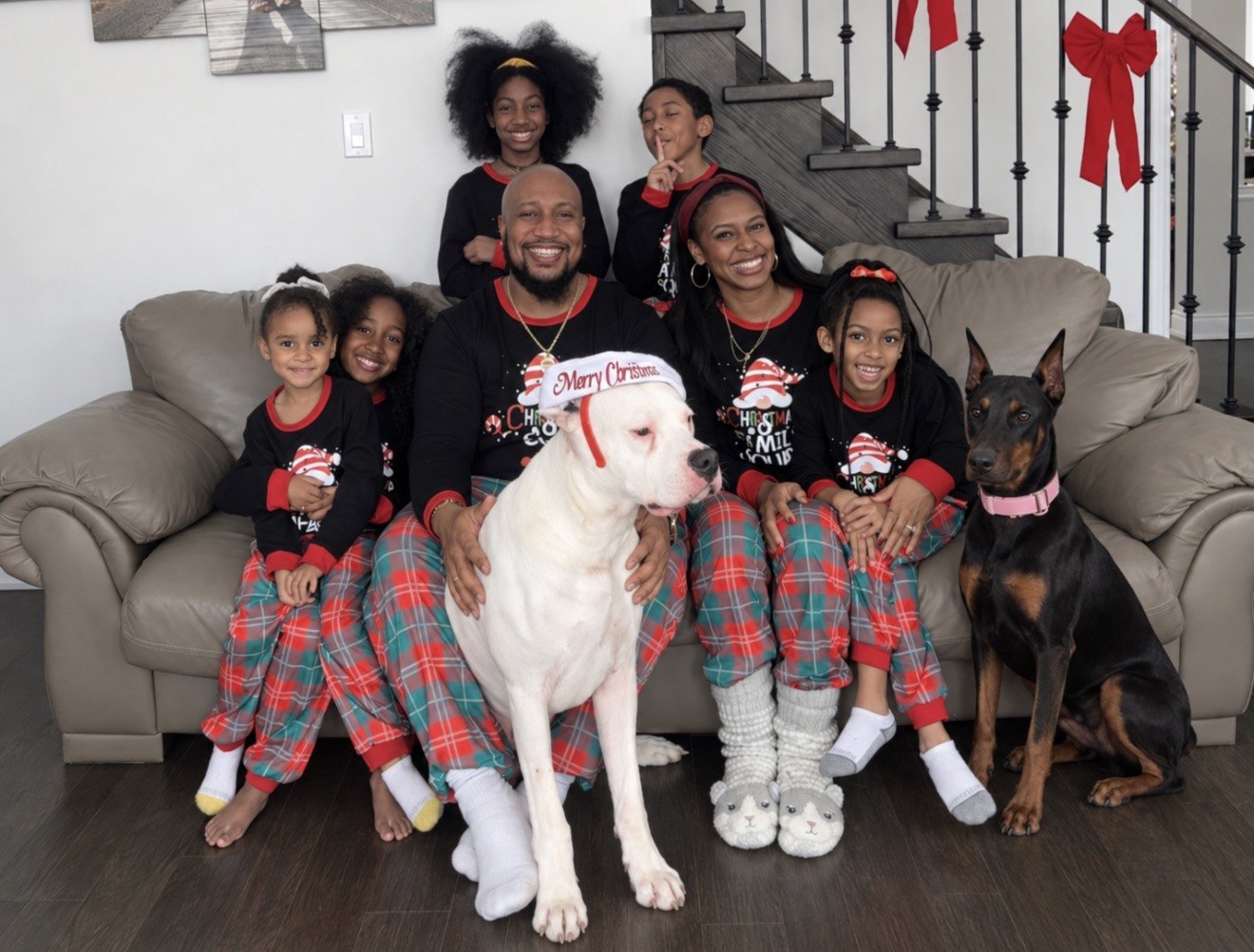 Andrew, his wife and their five children in matching Christmas pyjamas on a couch with their white dog in a Christmas hat and their Doberman